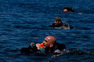 Νικώντας τα κύματα – Άντρας από τη Συρία κρατά στην επιφάνεια ένα μωρό, κολυμπώντας ταυτόχρονα προς την ακτή, στιγμές αφότου η λέμβος στην οποία επέβαιναν βούλιαξε εκατό μέτρα από τη στεριά (Λέσβος, 12 Σεπτεμβρίου 2015)