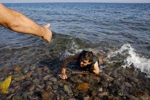Ενότητα - Κάτοικος της Λέσβου απλώνει το χέρι του στον Σύρο πρόσφυγα, που μόλις έχει εγκαταλείψει τη λέμβο, κολυμπώντας εξαντλημένος προς την ακτή (Λέσβος, 17 Σεπτεμβρίου 2015)