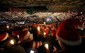Πλήθος, κρατώντας ανάμενα κεριά και φορώντας σκούφους Άγιου Βασίλη βρίσκονται σε συναυλία-γιορτή στο Βερολίνο.