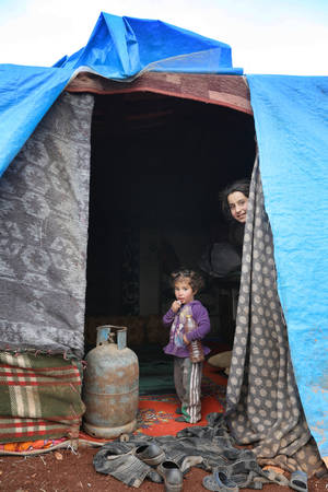 Δύο παιδιά κοιτάζουν έξω από την αυτοσχέδια σκηνή που είναι το νέο τους σπίτι. Οι κουβέρτες και το νάιλον είναι η μόνη προστασία που έχουν από το κρύο του χειμώνα. Έχουν μια μπουκάλα υγραερίου για να ζεσταίνονται, όμως δεν είναι ασφαλής η χρήση της μέσα σ