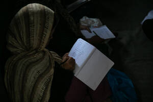 Μία γυναίκα γράφει στο τετράδιό της κατά τη διάρκεια μαθήματος αγγλικών σε μία αυτοσχέδια αίθουσα διδασκαλίας.