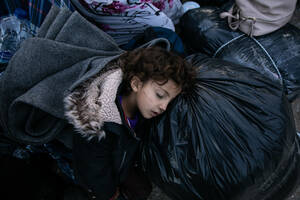 Ένα κορίτσι κοιμάται πάνω σε σακούλες με πράγματα, περιμένοντας το λεωφορείο. Είναι άλλοι 200 «τυχεροί» που θα αφήσουν πίσω τους τη Μόρια.
