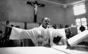 2004, Αϊτή. Ο Πρόεδρος της χώρας, Ζαν-Μπερτράντ Αριστίντ φεύγει από τη χώρα, μετά από μια αιματηρή εξέγερση. Ο Αριστίντ υπήρξε παπάς και στη φωτογραφία φαίνεται να λειτουργεί, το 1988. Η προεδρία του έφερε την Αϊτή σε οριακή κατάσταση και την πλειοψηφία τ